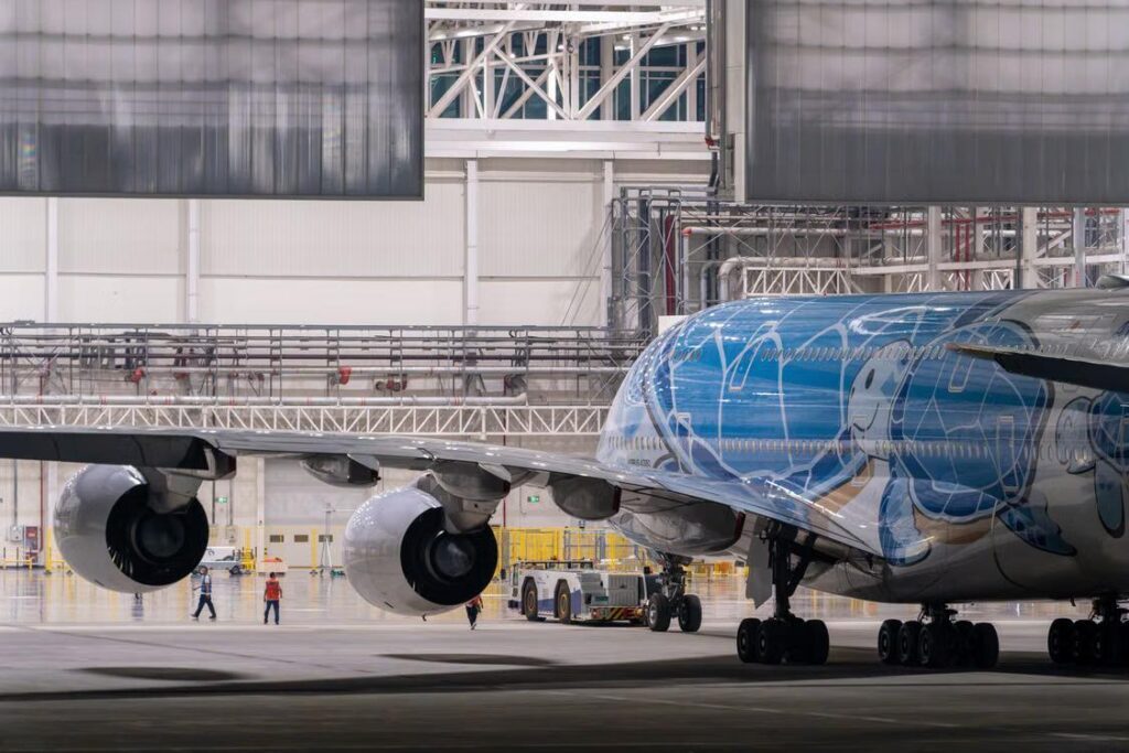 A vividly painted aircraft parked inside a spacious hangar with engineers nearby